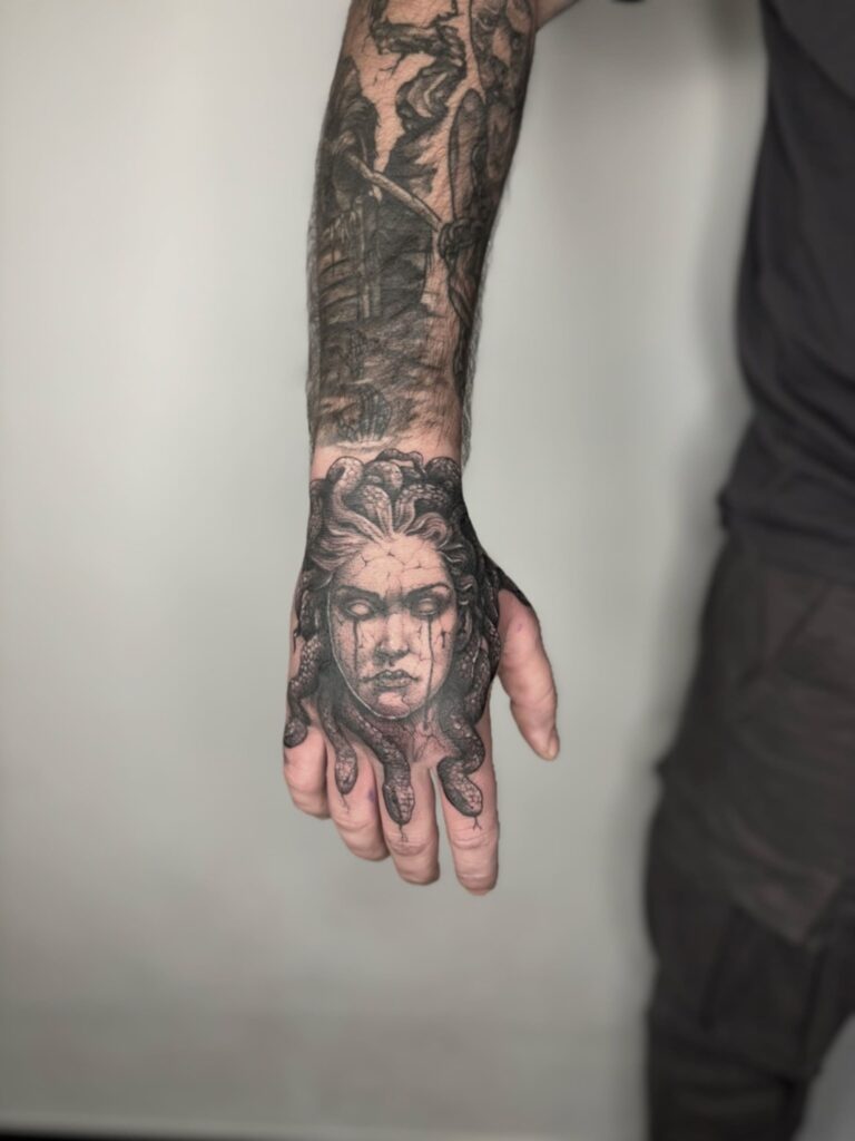 Twarz Meduzy pokrywająca całą dłoń, z wężowymi palcami – rozbudowana, mroczna kompozycja w stylu dotwork